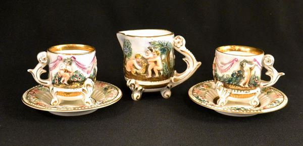 Due tazzine con piattini e lattiera, sec. XX, in ceramica Capodimonte policroma, decorata con putti a rilievo, alt. cm 6 e cm 8&nbsp;&nbsp;&nbsp;&nbsp;&nbsp;&nbsp;&nbsp;&nbsp;&nbsp;&nbsp;&nbsp;&nbsp;&nbsp;&nbsp;&nbsp;&nbsp;&nbsp;&nbsp;