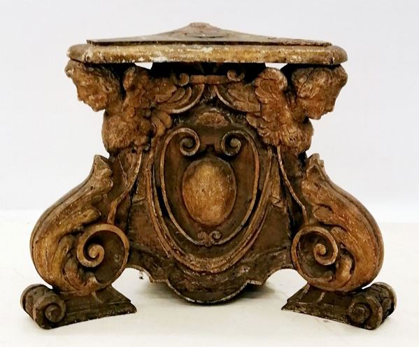 Basamento di torciera, sec. XVIIin legno intagliato, piano triangolare a becco di civetta sotteso da cherubini ed ampie volute ad inquadrare motivo araldico, piedi a ricciolo, alt. cm 49, difetti 