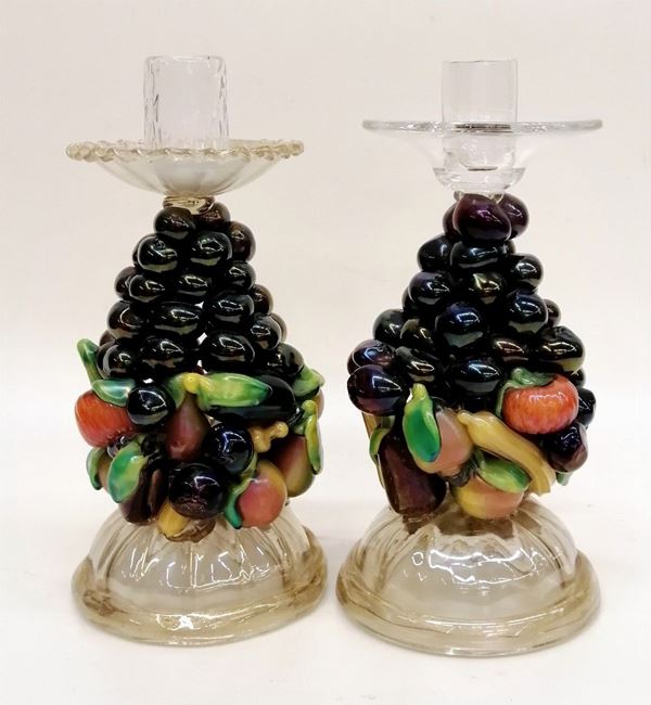 



Due candelieri, Murano, sec. XX, in vetro trasparente incolore con&nbsp; inclusioni auree, fusto decorato con frutta policroma, alt. cm 25 e cm 26 ( 2 )