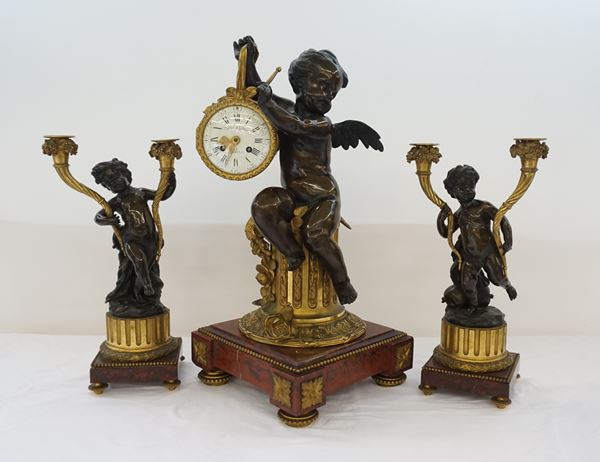 Trittico, Francia, sec. XIX, composto da orologio e coppia di candelieri in bronzo forgiato a putti, basi in marmo, orologio cm 42x62, candelieri cm 24x45 ( 3 )