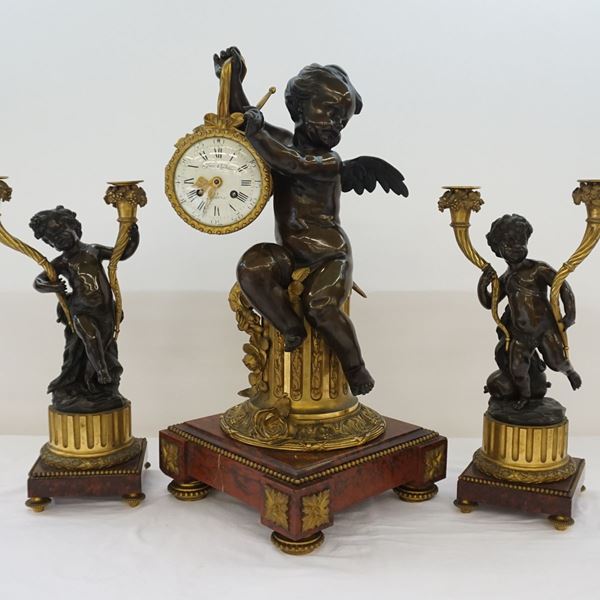 Trittico, Francia, sec. XIX, composto da orologio e coppia di candelieri in bronzo forgiato a putti, basi in marmo, orologio cm 42x62, candelieri cm 24x45 ( 3 )